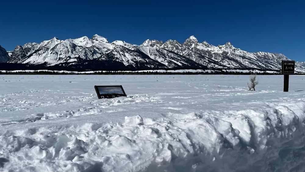 Snow-capped mountains under a bright blue sky, with a snowy plain in the foreground 