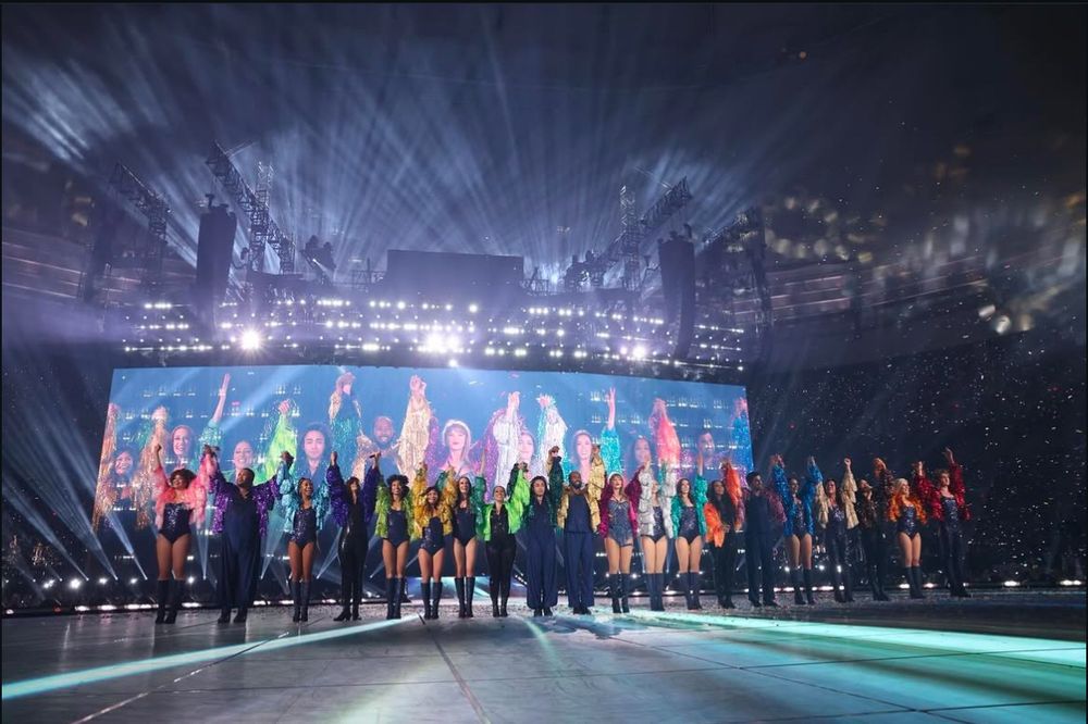 A photo of Taylor Swift with all of her backup dancers on stage at The Eras Tour preparing to take their final bow