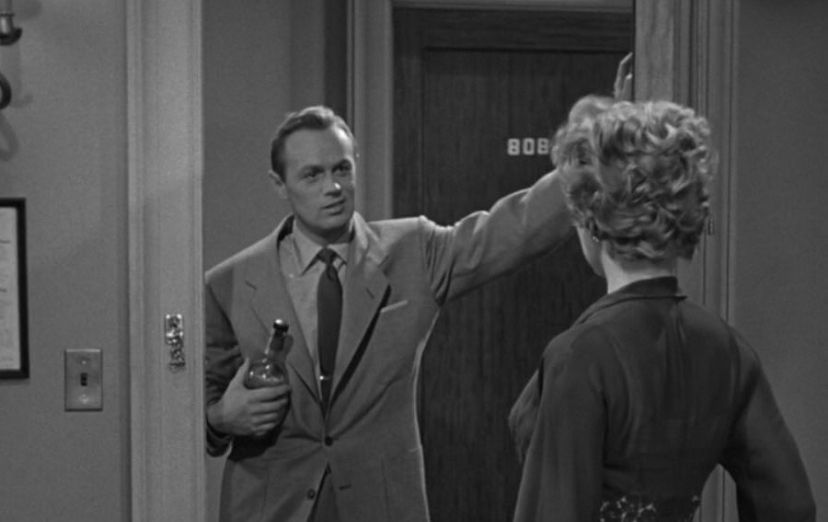 Black and white photo of Richard Widmark holding a bottle and leaning in a doorway