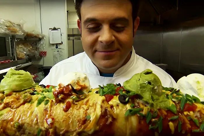 Adam Richman from Man vs Food staring lovingly at the B3 “Big Badass Burrito” from NASCAR Café at the Sahara Hotel and Casino in Las Vegas, NV. 
In Man v. Food Season 2, Adam becomes one of only three people to take down this 6-pound, 2-foot, 5,000-calorie burrito in 90 minutes, earning him free rollercoaster rides for life. 