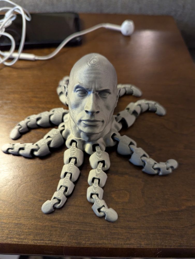 Grey 3d-printed item with octopus tentacles and a Dwayne "The Rock" Johnson head where an octopus head would be. He has the classic one eyebrow raised. 