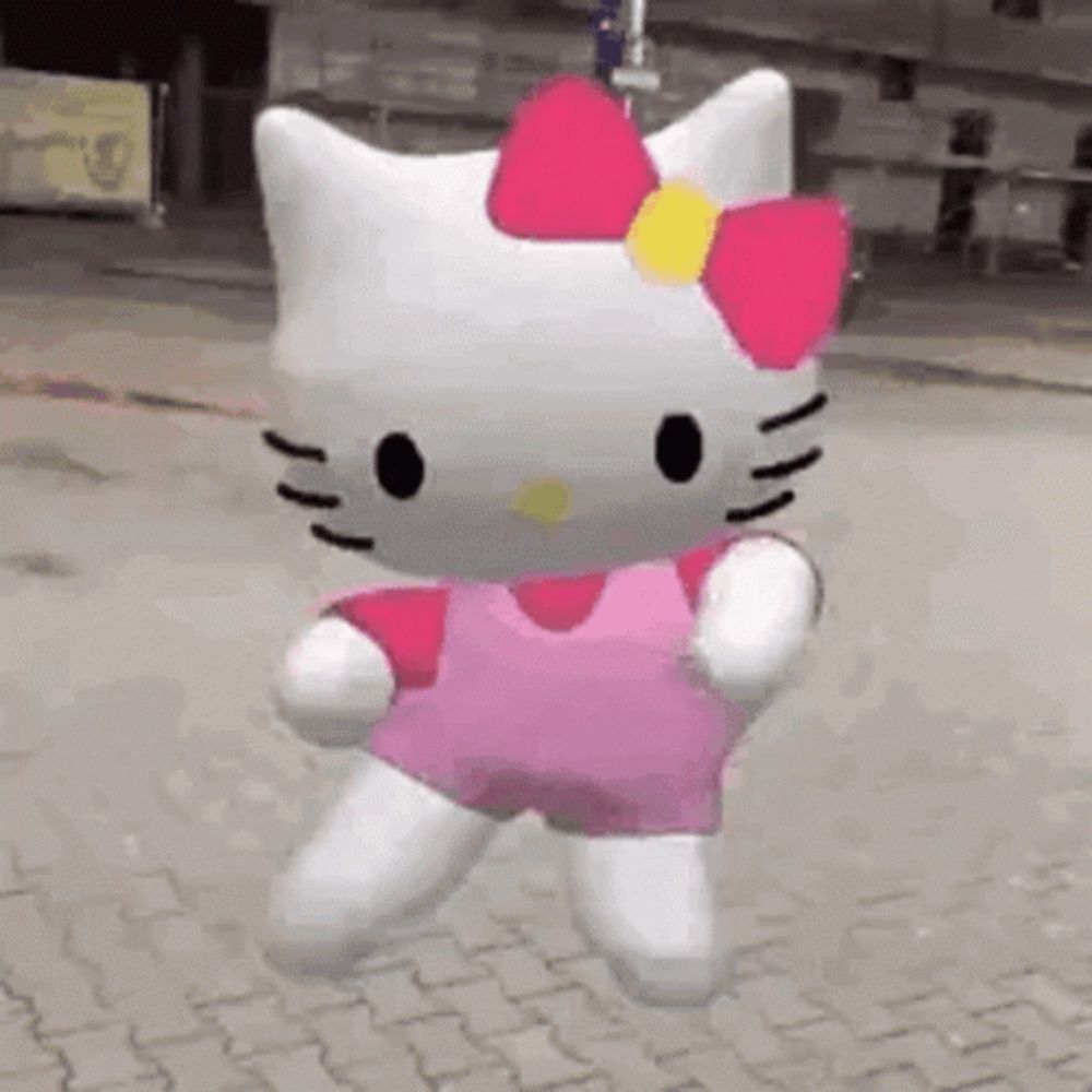 a hello kitty doll is standing on a sidewalk wearing a pink dress .