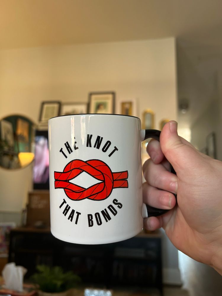 My hand holding a coffee cup that says “the knot that bonds”