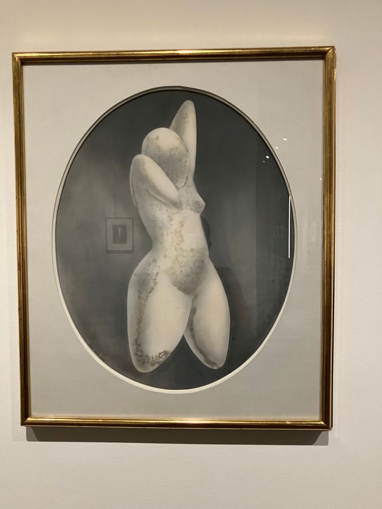 A framed oval aerograph by Man Ray titled Hemaphrodite, made using airbrush technique depicting a smooth featureless torso/body that appears almost like a marble sculpture.