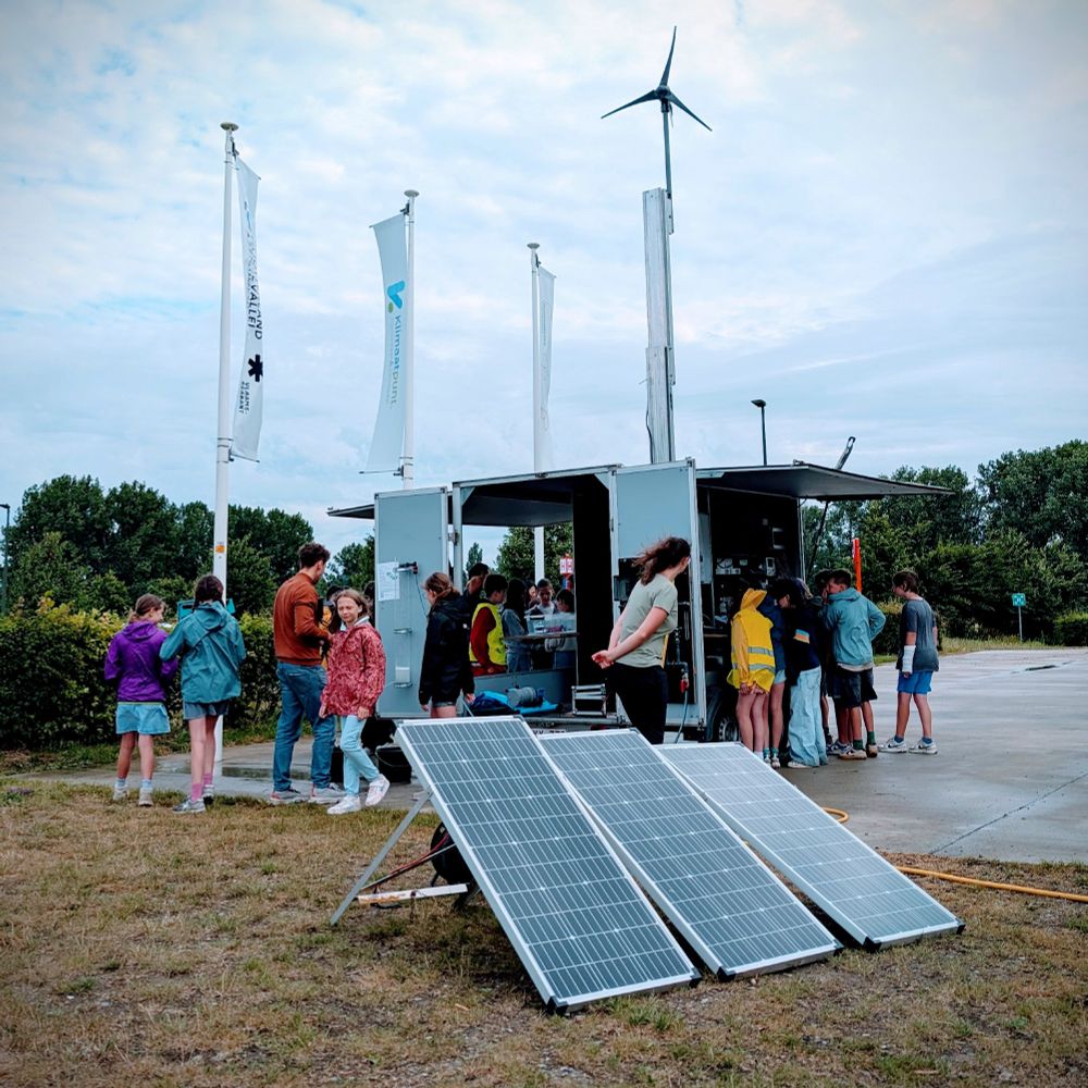 picture of kids around a truck with wind turbine on roof and solar panels in the grass - cloudy sky