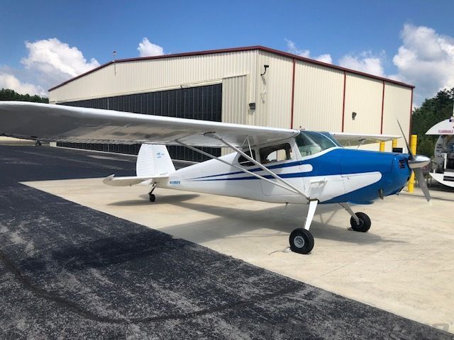 A blue-over-white 1948 Cessna 170 parked on a concrete ramp outside a hangar