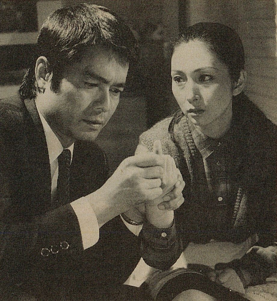 Black and white image of Hiroshi holding Meiko's hand and looking at it while Meiko looks at him.