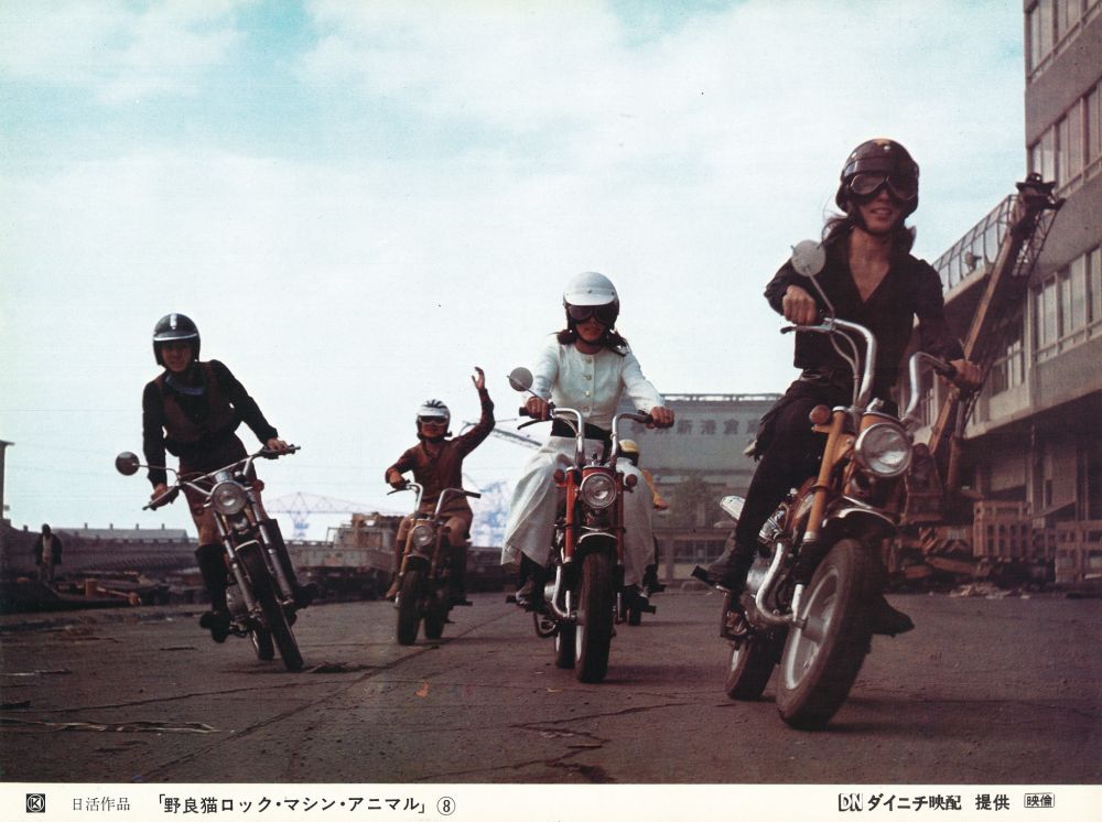 Four women on motorcycles, in varying distances from the camera.