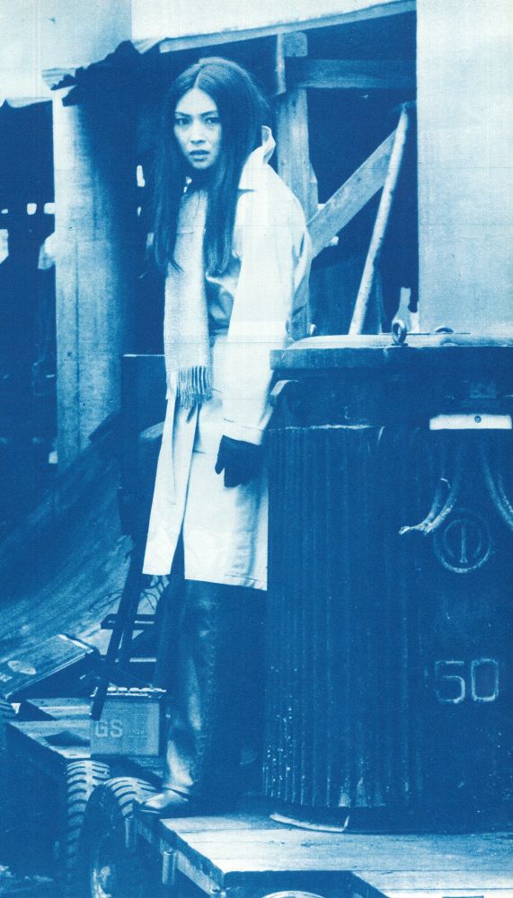 Blue and white image of Meiko in a long, white coat with a shotgun in her hand, pointing down. She's standing on a loading dock or something similar.