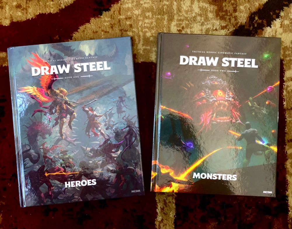 The Heroes book and Monsters book, for the Draw Steel game by MCDM, sitting side by side. 