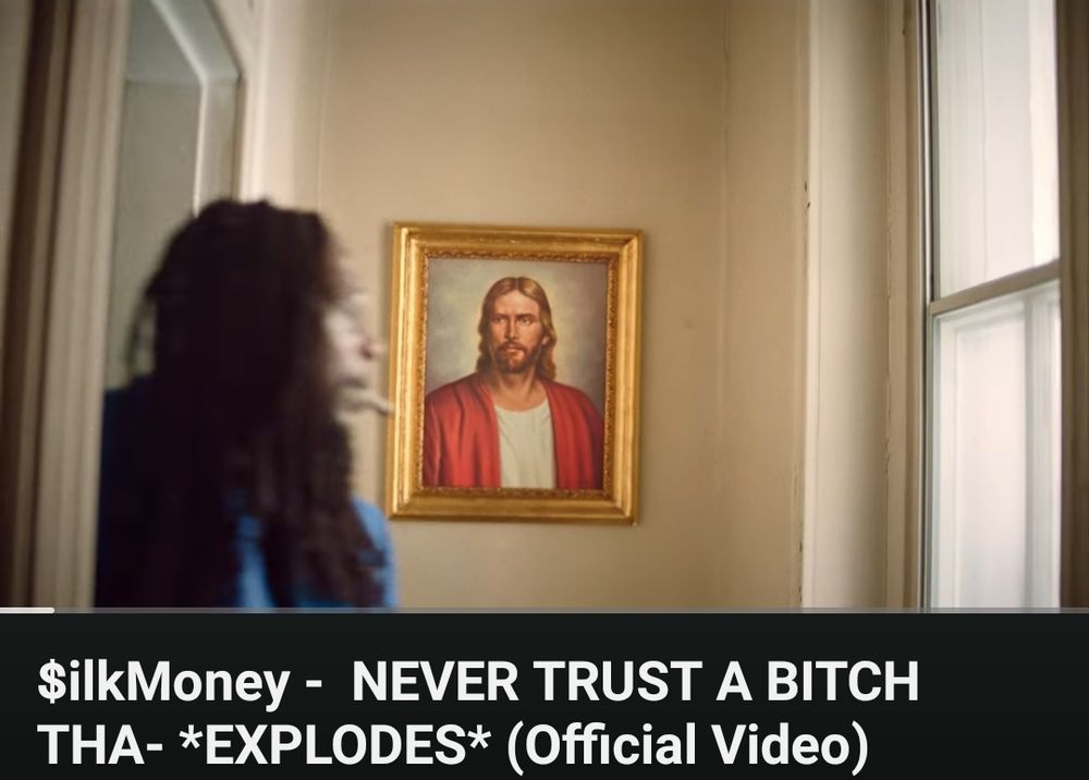 A screenshot of VA rapper $ilkmoney casually strolling past a painting of Jesus in the music video for "NEVER TRUST A BITCH THA- *EXPLODES*" off his latest full length LP "WHO WATERS THE GIVING TREE ONCE THE LEAVES DRY UP AND FRUITS NO LONGER BEAR?"