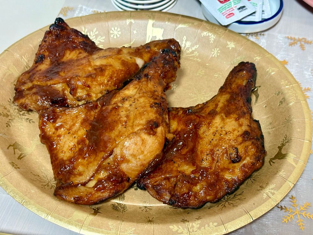 크리스마스 파티의 바베큐 치킨. 금색 종이 접시 위에 갈색 소스가 버무려진 닭다리 3개가 올라가 있습니다.