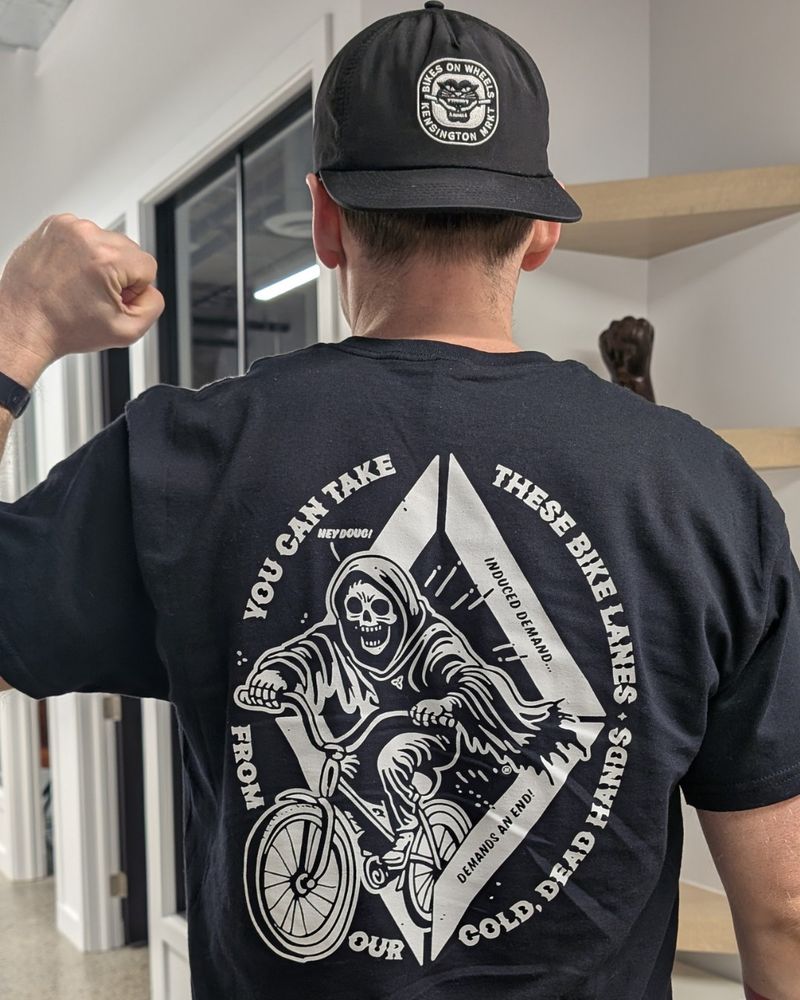 person with black hat and shirt photographed from behind with raised fist.