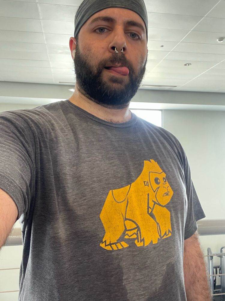 Selfie of sweaty me with my tongue out at the gym, and I’m wearing a t-shirt with a cartoon gorilla on it.