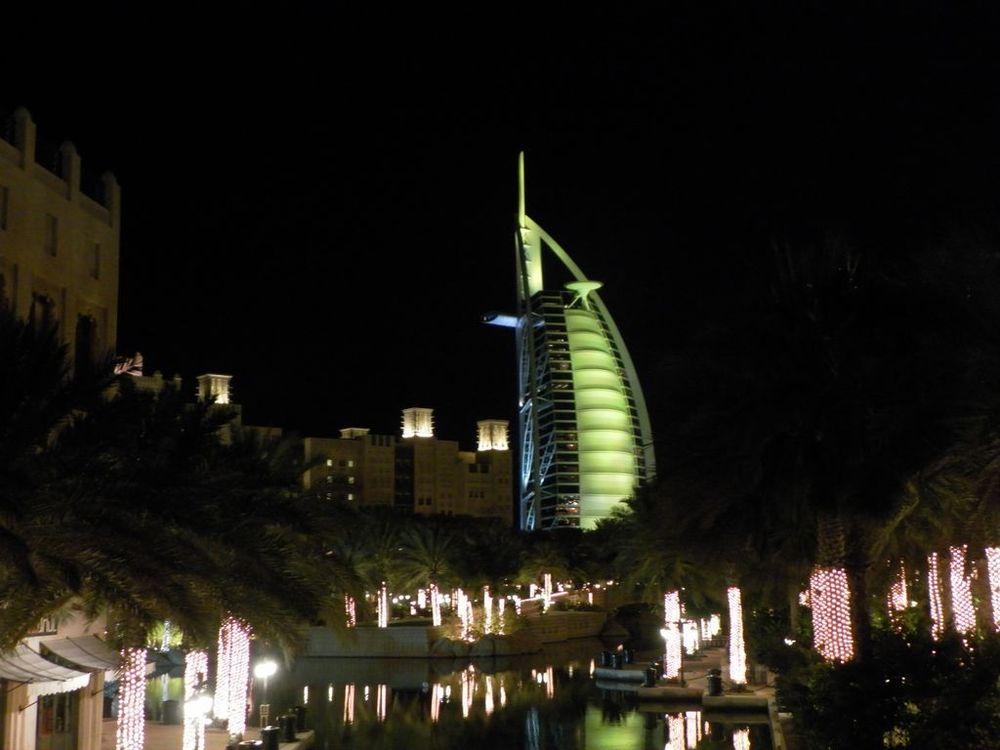 das Hotel Burj al Arab in Dubai leuchtet grün und darunter befinden sich Palmen mit tausenden weissen LED-Lichtern