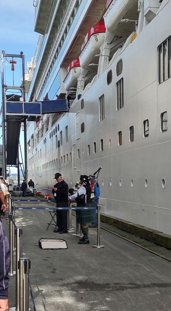 a bagpipe player next to the side of a white cruise ship.