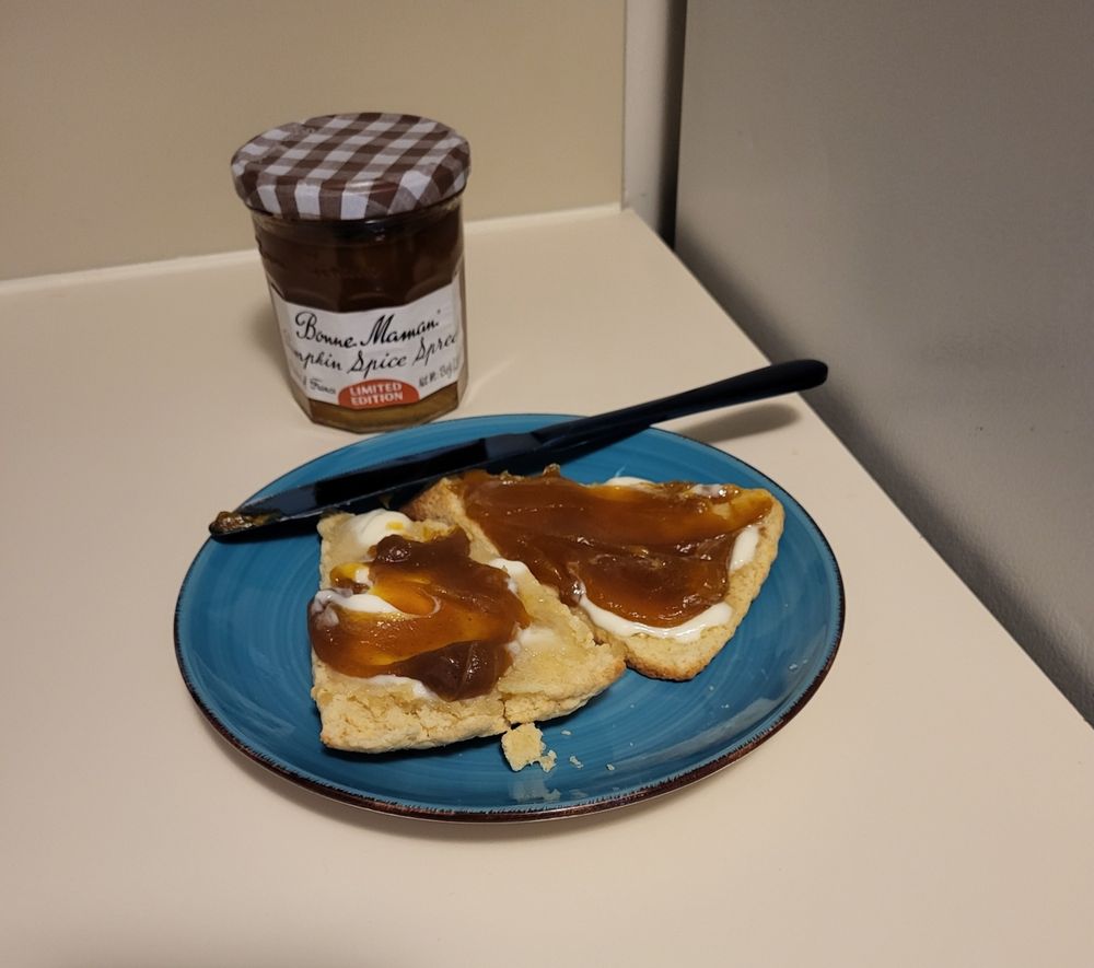 A hot scone right out of the oven spread with butter and pumpkin butter (a cooked pumpkin compote that has no dairy in it) on a blue plate.