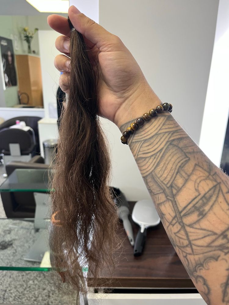 Mão segurando um pedaço de aproximadamente 40cm de cabelo cortado em um salão