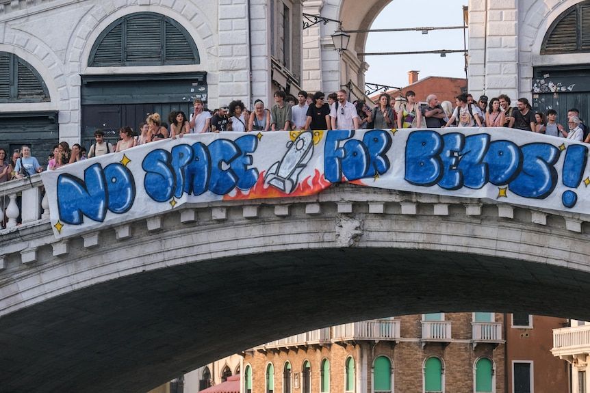 a stone bridge crowded with people, there's a banner on the side reading NO SAPCE FOR BEZOS with a lil rocket ship drawn on it

it's ponte di rialto in venice