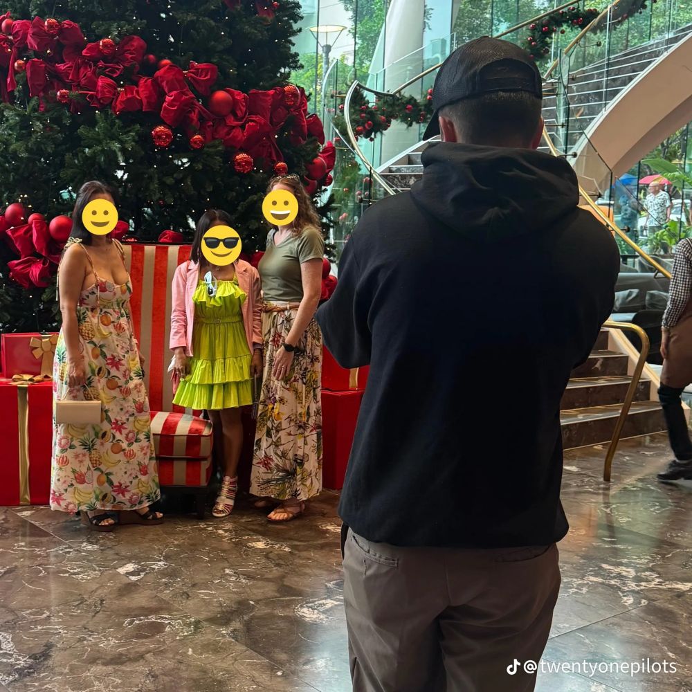 An image of Tyler Joseph helping a trio of young women take a picture in front of a large Christmas tree. 