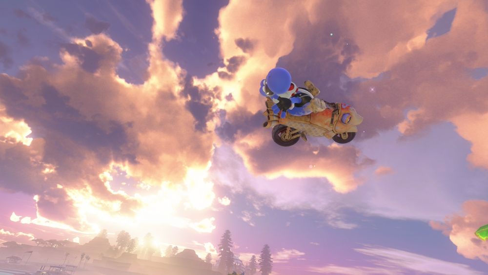 Screenshot from Mario Kart World. Blue Yoshi in a biker outfit doing a trick in the air. The background is an almost-sunset with a pretty pattern of clouds spread across it.
