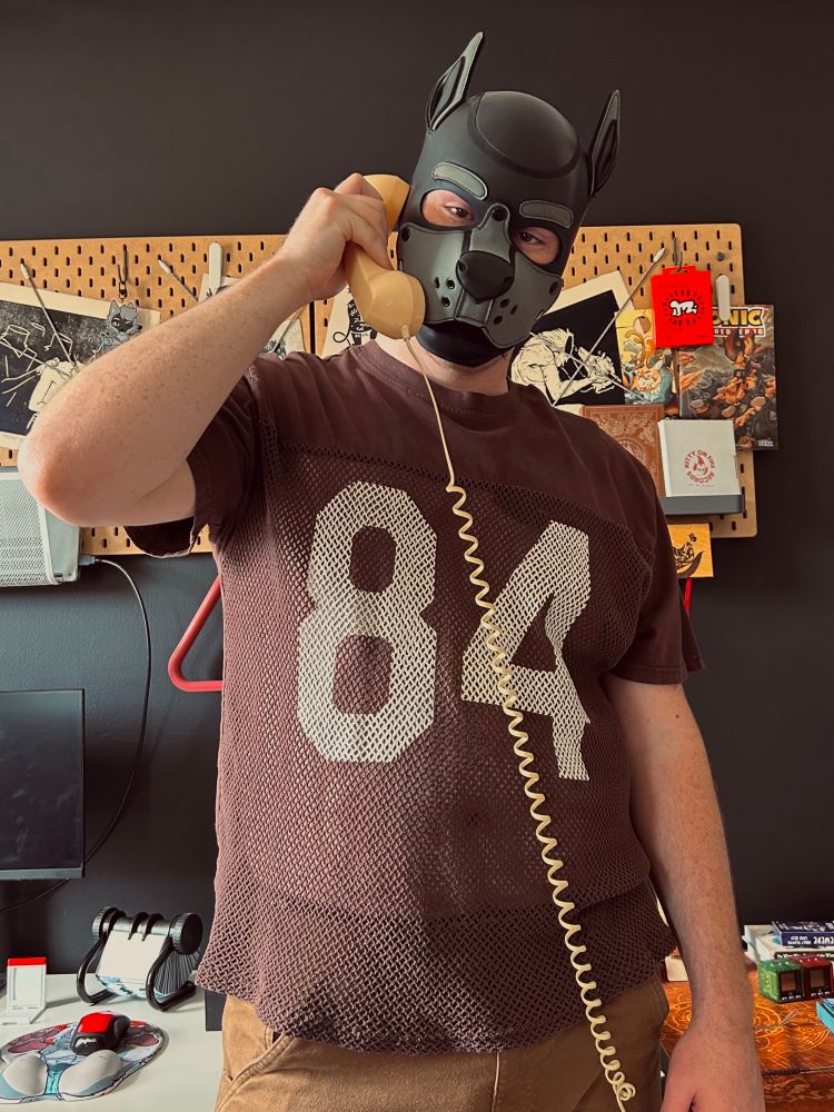 a man in a dog mask weeding a football jersey and holding a corded phone to his ear