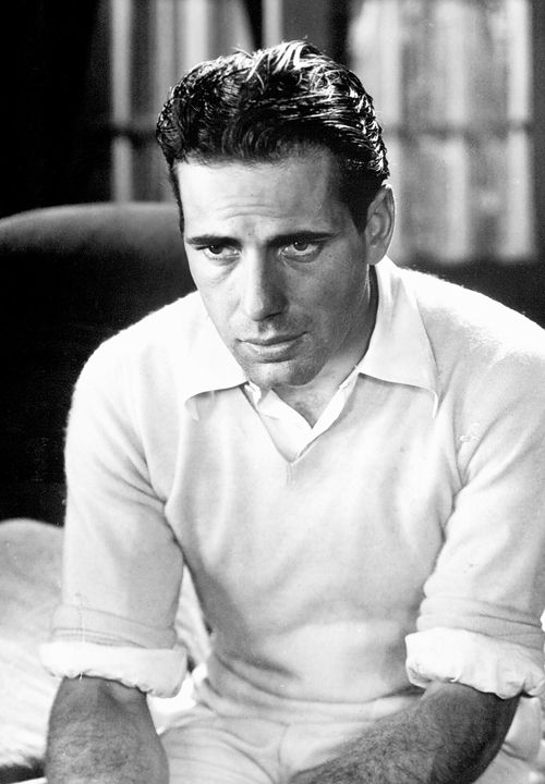 Young Humphrey Bogart in open-collar shirt and light sweater, sleeves rolled up. 