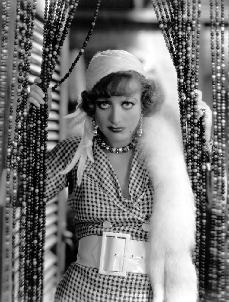 Joan Crawford, in full tarted-up costume and makeup as Sadie Thompson in RAIN, peers through a beaded curtain in this publicity still (b&w)