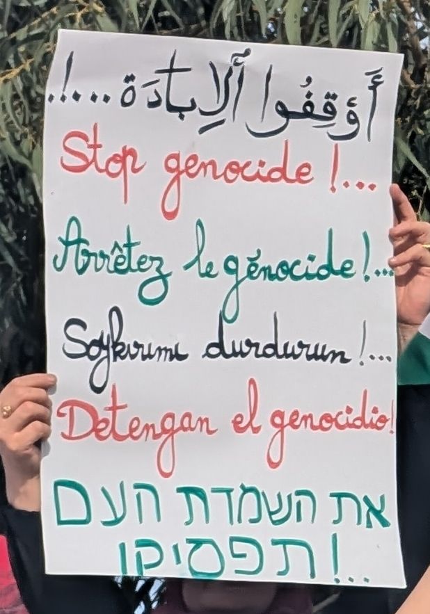 A poster saying "Stop genocide" in Arabic, English, French, Turkish, Spanish and Hebrew, using black, red and green marker 