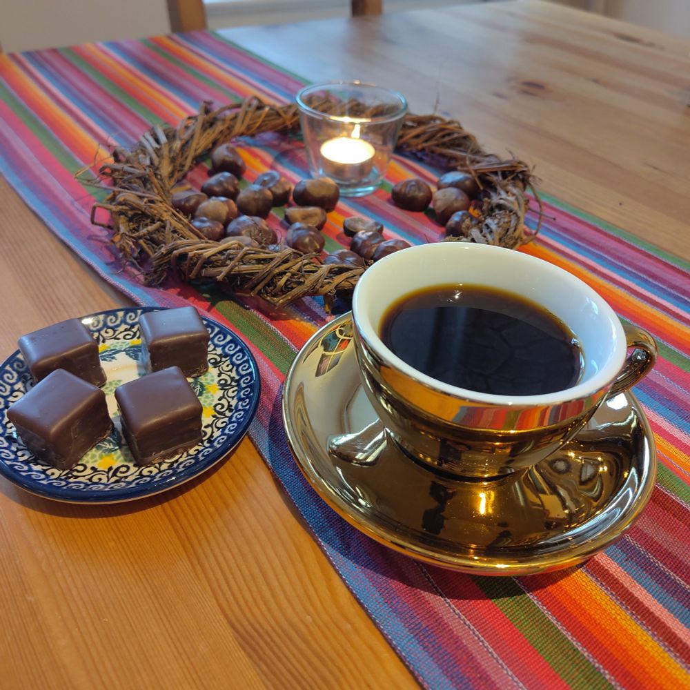 A table with colorful tablecloth, a golden cup of coffee and sweets.
