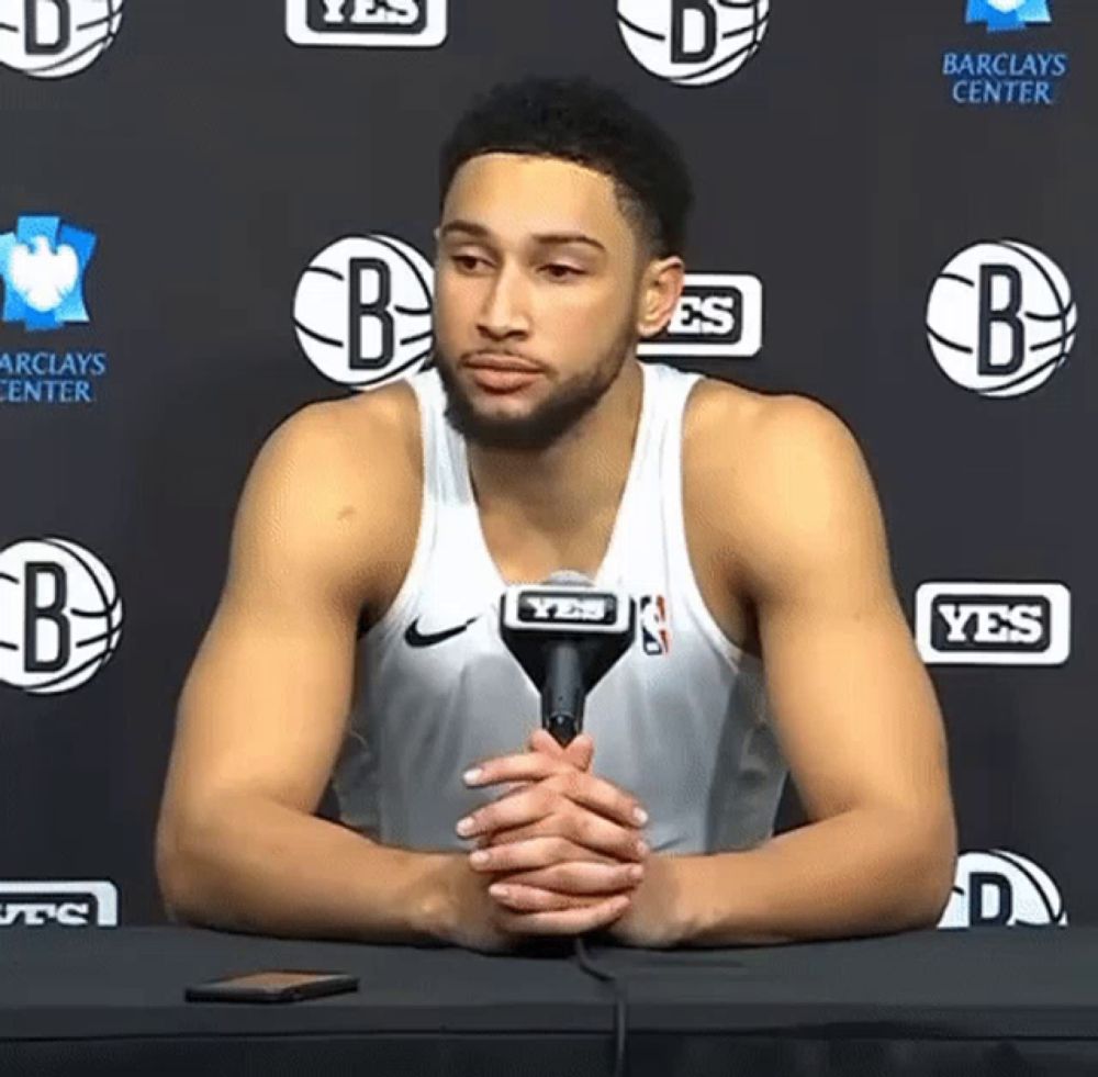 a basketball player is sitting at a table with a microphone in front of a wall that says yes