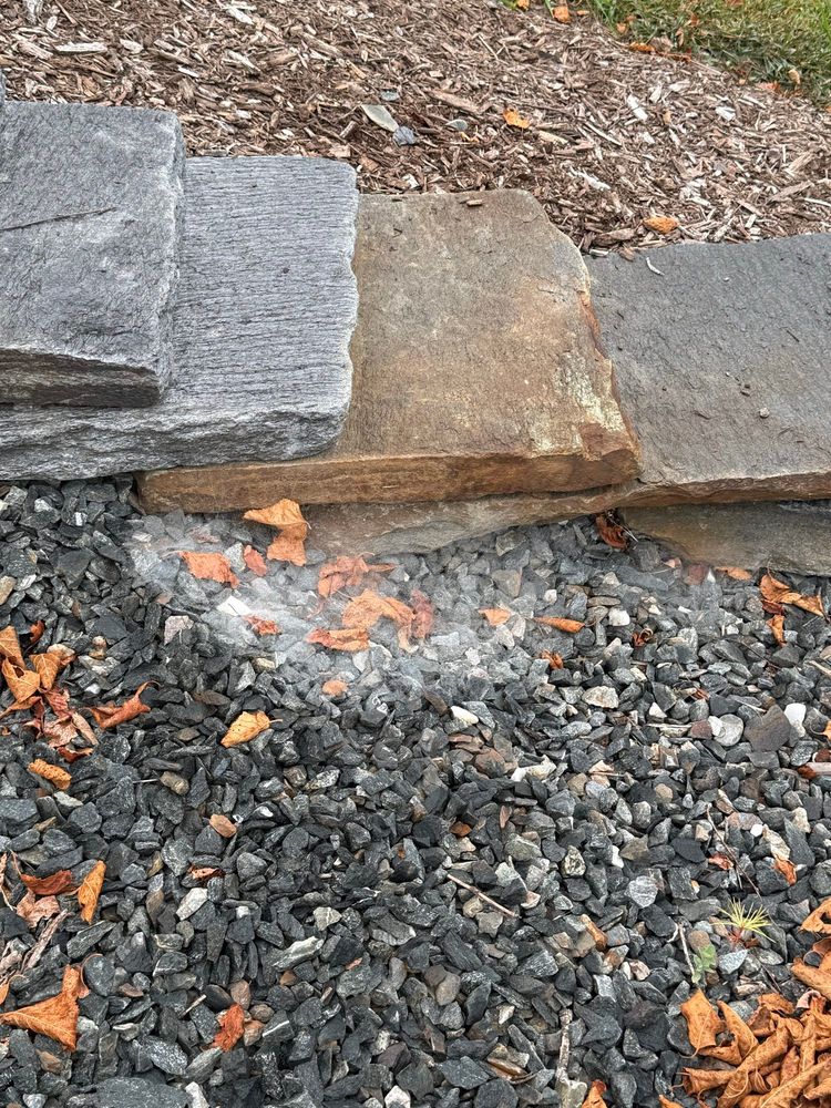 A stone walkway, with a white spiderweb next to it, resembling a little cloud of cotton. There are stones on one side of the walkway and mulch on the other.