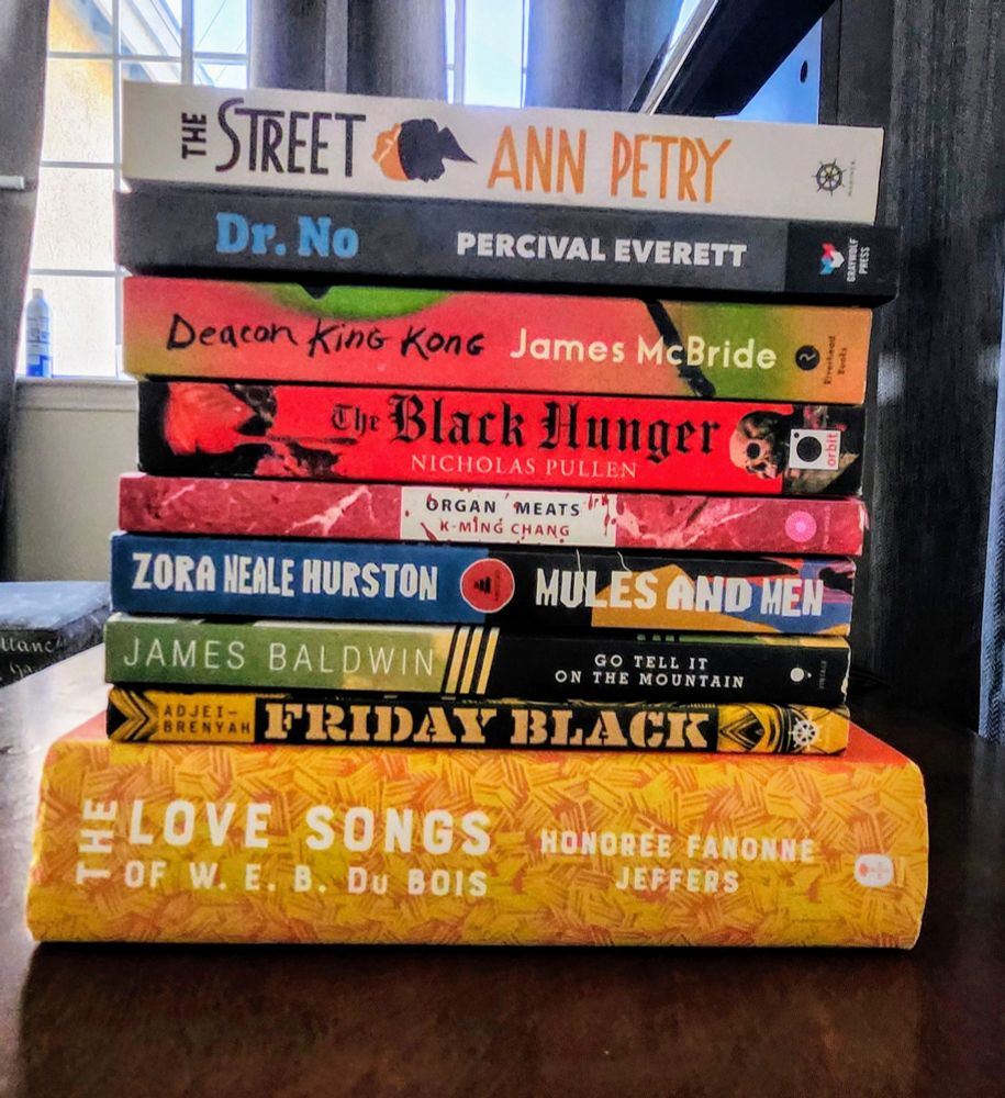 Pictured is a stack of books.

The Street by Ann Petry
Dr. No by Percival Everett 
Deacon King Kong by James McBride
The Black Hunger by Nicholas Pullen
Organ Meats by K-Ming Chang
Mules and Men by Zora Neale Hurston
Go Tell It On the Mountain by James Baldwin 
Friday Black by Nana Kwame Adjei-Brenyah
The Love Songs of W.E.B Du Bois by Honorée Fanonne Jeffers