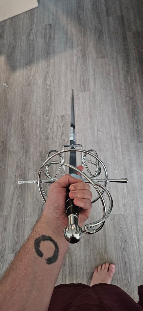 a long silver blade with a wrapped hilt is held in the hand with the point down