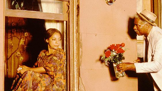 Mother Sister (Ruby Dee) sits in her window as Da Mayor (Ossie Davis) hands her a bouquet of roses.