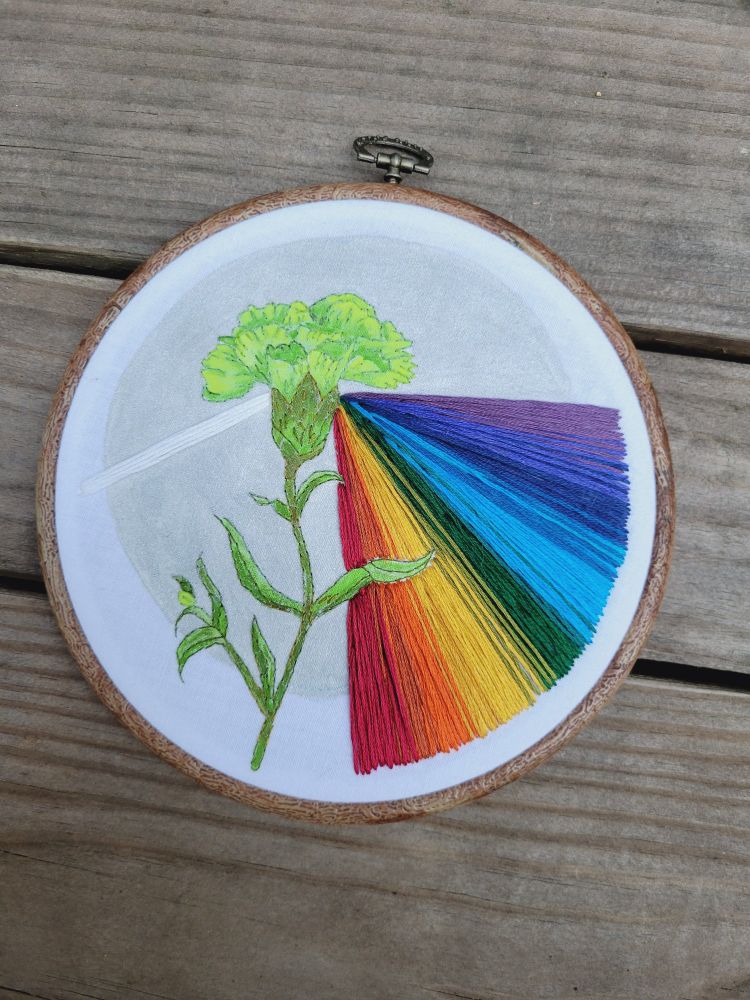 A painted embroidery piece depicting a painted green carnation and a stitched rainbow prism against a silver painted backdrop