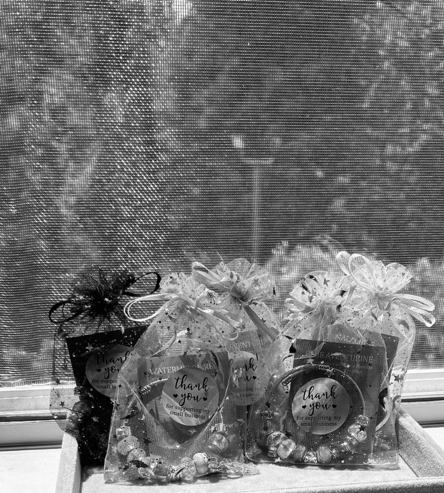 A mono toned photo of European beaded bangles from my shop, Starlit Oddities, and are made by me. They’re crystal themed and mono toned to not spoil the pattern or colors for buyers! They’re in front of a window screen for the lighting and inside of a gray jewelry display tray. There’s holographic ‘thank you for supporting my small business’ stickers on each celestial themed organza bag with tiny hearts. The bag strings are tied into bows. Everything is a different color when the mono toned filter is removed. Thank you for supporting me. 