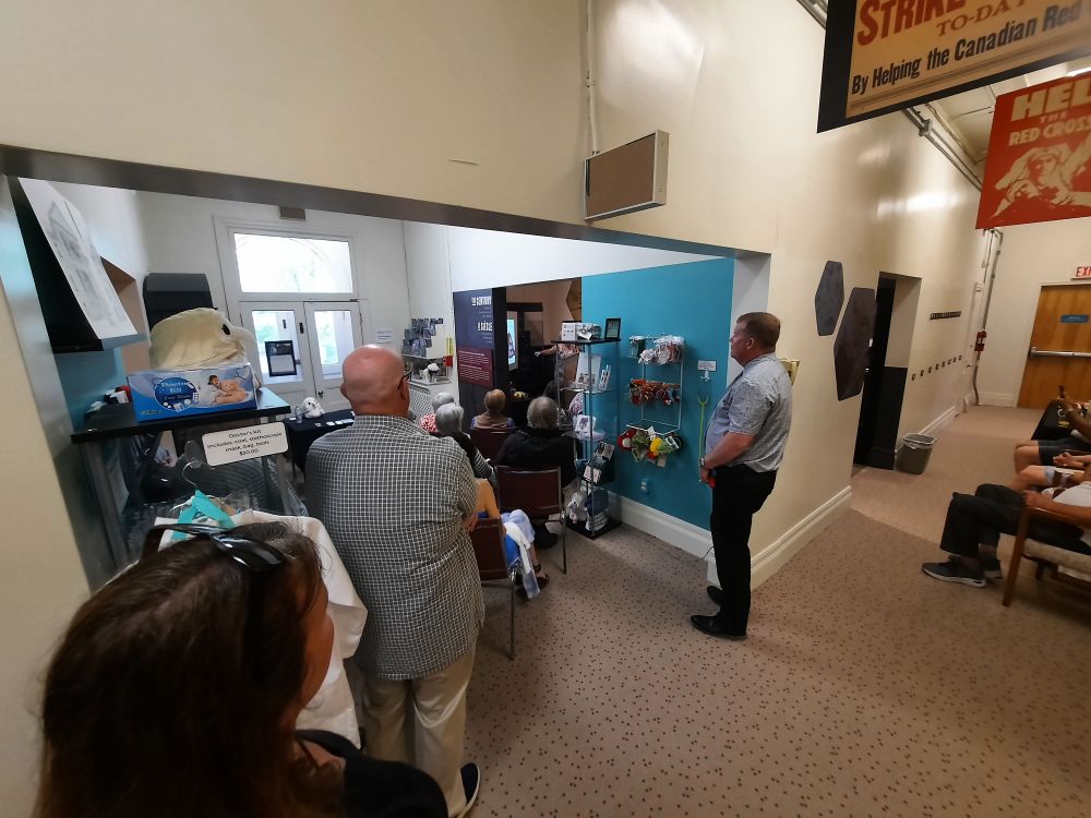 People sitting and standing in the halls of the museum of healthcare, all looking into another room.