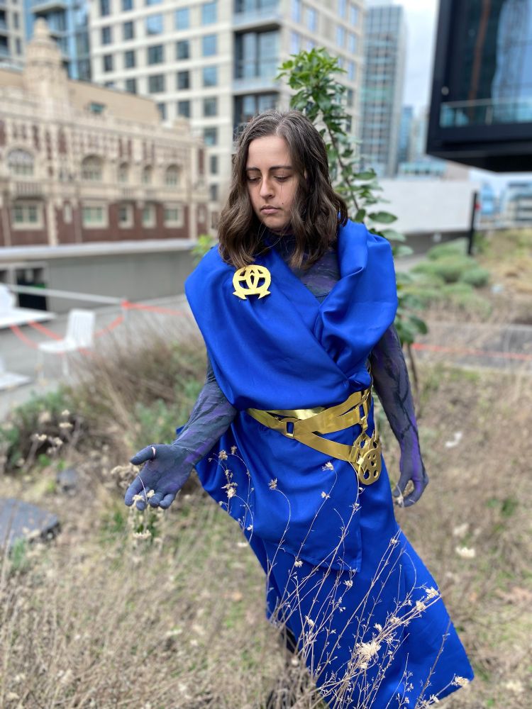 Cosplay of Viktor from Arcane, blue robe and gold belt, looking at a dying plant