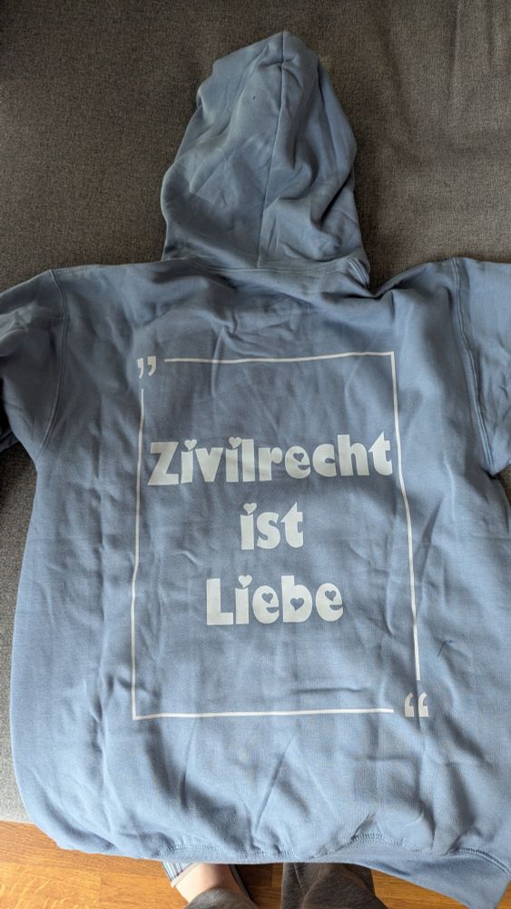 Ein himmelblauer Hoodie. Auf der Rückseite steht in weißer Schrift „Zivilrecht ist Liebe“. 