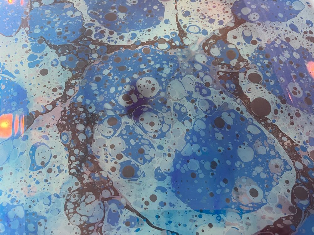 Splotchy patterns of blue and black paint float on top of the “size” for marbling paper