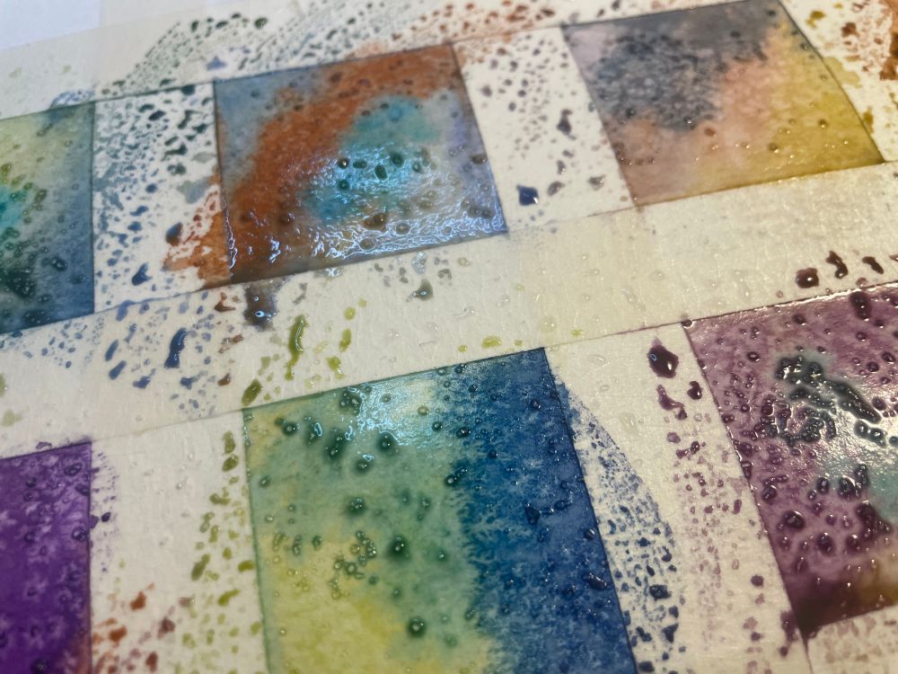 Square shaped small watercolor paintings with varying colors and splotchy shapes, masking tape blocks off the square painted areas on the paper