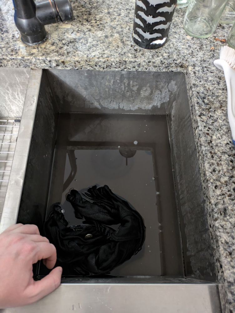 A black vest being washed in a sink. The water is dark gray with dirt. 