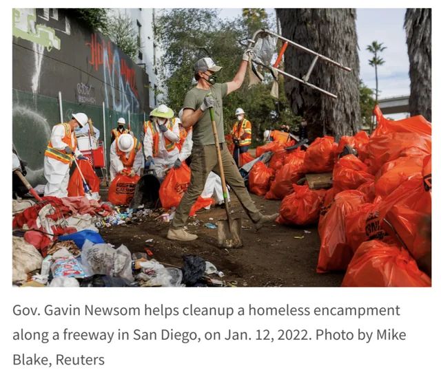 A photo of Newsom holding up a walker. Caption reads: "Gov Gavin Newsom helps cleanup [sic] a homeless encampment along a freeway in San Diegon, on Jan. 12, 2022. Photo by Mike Blake, Reuters.