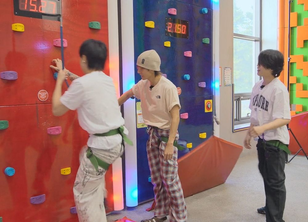 Jungkook, Jimin and Taehyung at an indoor climbing wall from Are You Sure.  Jungkook is about to climb, and Taehyung and Jimin are standing back watching him.