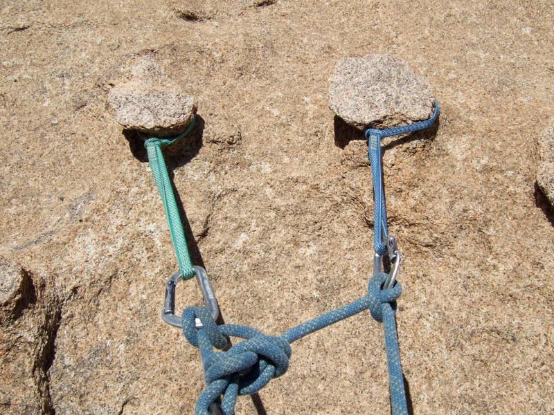 Two chickenheads that are used to form an anchor for a climb, which is the main part of the climbing system that protects the climbers from falling.  In this anchor, two slings are girth hitched around the thinner parts of the chickenhead, close to the wall, such that they won't slip off.  The climbing rope is then tied to those slings.