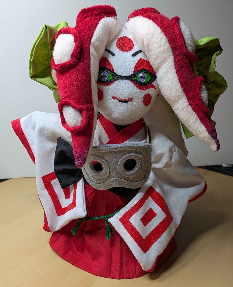 Full body picture of a handmade plushie of a Splatoon oc who happens to be a female Octoling dressed in kabuki inspired attire. There are a pair of goggles around her neck. She has been made with a lot of love and care.