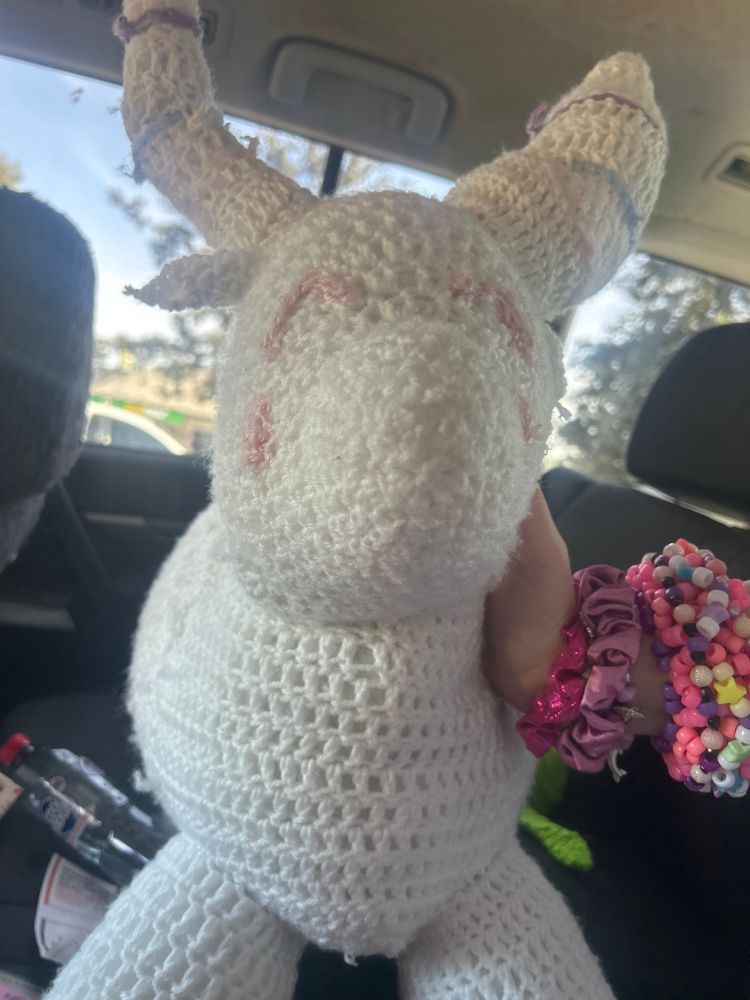 The front view of a white crochet impala plushie with pink eyes and blush, the stripes on its horns are different colours.