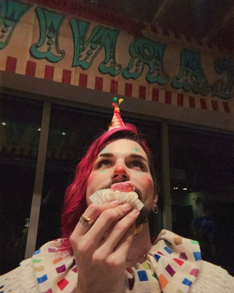 a photo of me dressed up as a clown holding a circus animal cookie dessert in front of a banner that reads “CARNIVAL”