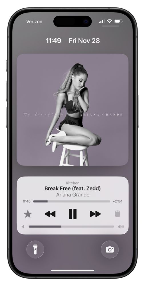 iPhone lock screen showing a music player with Ariana Grande’s My Everything album cover. The cover features Ariana sitting on a white stool against a lavender background. The song “Break Free (feat. Zedd)” is playing, and the lock screen displays the time 11:49, date Fri Nov 28, and flashlight and camera icons at the bottom.